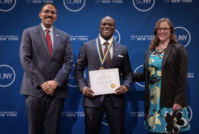 A student holding a certificate poses for a photo with two others at each of his sides.
