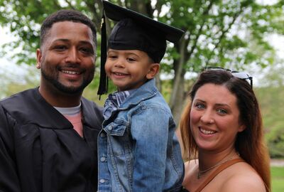 Two people, one wearing graduation gown, hold a child wearing graduation cap.