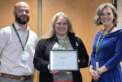 A person holds a certificate of achievement with two others posing on both sides.