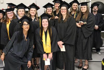 A group of student graduates in cap and gown pose together.