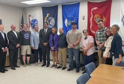 A large group of people smile while posing in a college veterans lounge.
