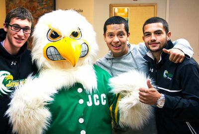 Three college students pose with the JCC Jayhawk mascot.