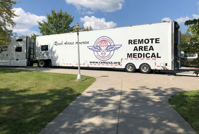 A large Remote Area Medical semi truck parked outside near a sidewalk and grassy area.