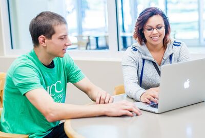 Two people smiling and working together on a laptop at a table. 