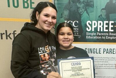 A smiling woman and child pose together. The woman holds a certificate. Behind them, a banner about education for single parents.