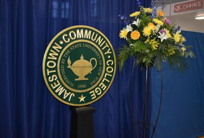 Seal of Jamestown Community College displayed next to a colorful bouquet of flowers against a blue curtain backdrop. 