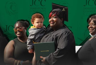 Graduate in cap and gown holds a diploma and a toddler, smiling alongside two women. Jamestown Community College backdrop, celebratory atmosphere.