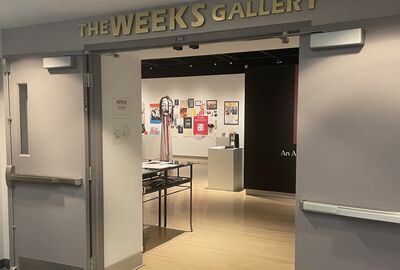 The open entrance to The Weeks Gallery reveals a quiet exhibition space with framed posters, display tables, and a central pedestal.